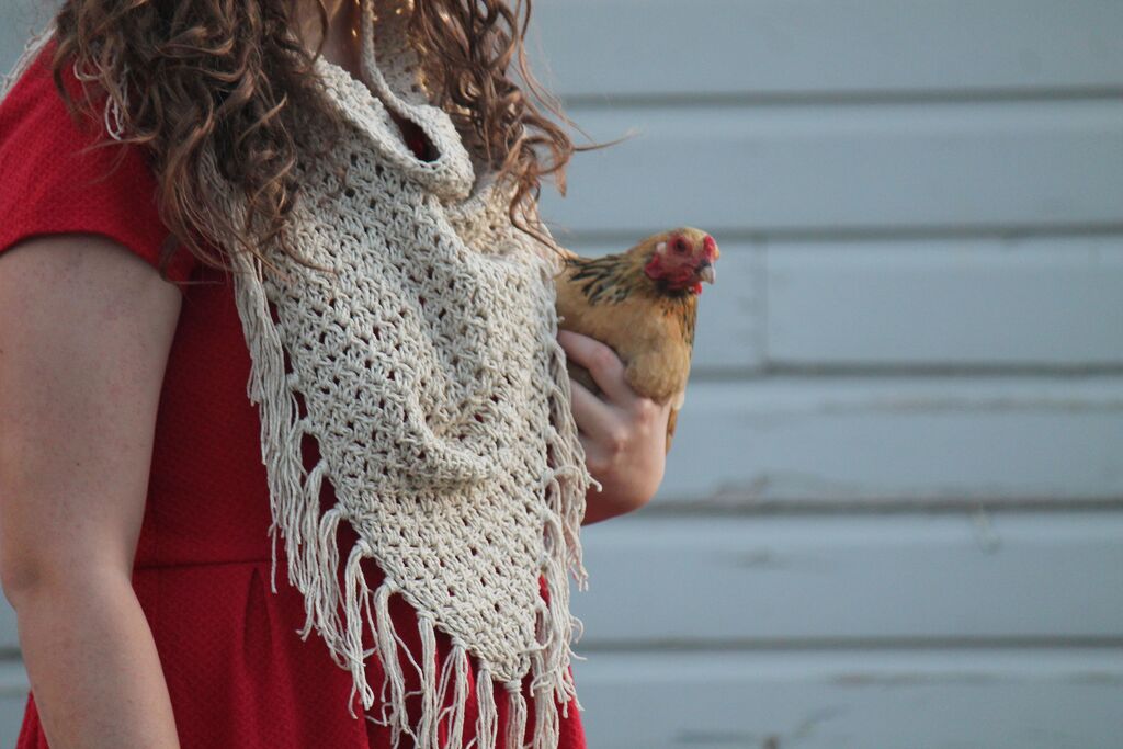 Model in red dress and fringed crochet cowl holding a chicken.