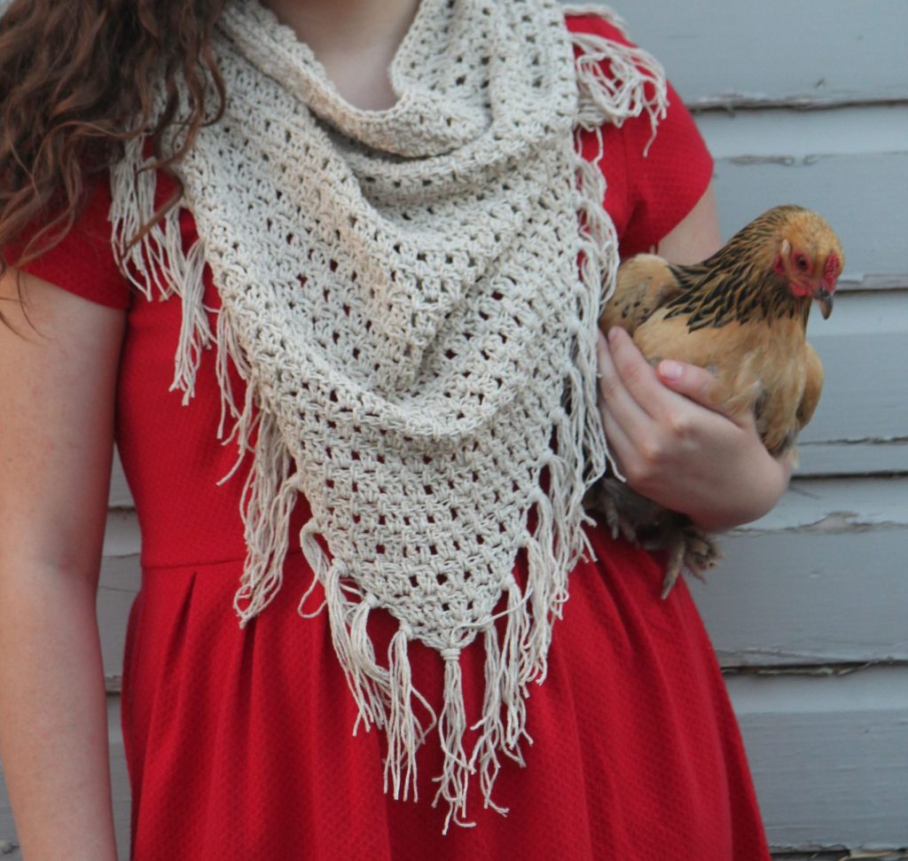 Model in red dress and fringed crochet cowl holding a chicken.